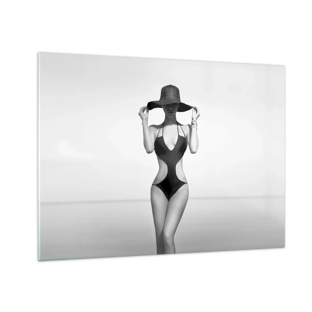 Billede på glas - En kvinde i sort badedragt og hat mod havet - 70x50cm - Mit navn er Elegance - Moderne vægdekoration til stue og soveværelse ARTTOR