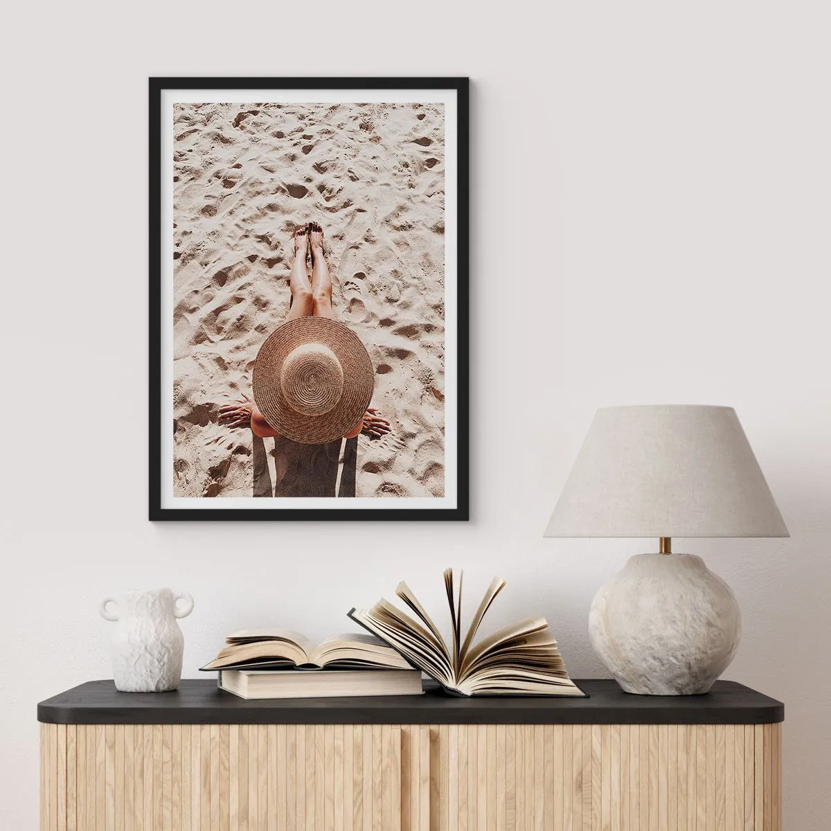 Plakat i sort ramme - Person solbader på stranden, set ovenfra med en stor hat mod sandet - 50x70cm - En drømmes tid - Moderne vægdekoration til stue og soveværelse ARTTOR