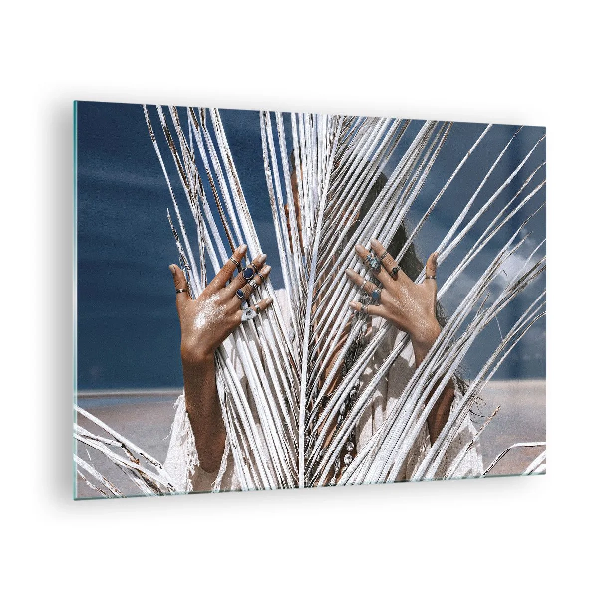 Billede på glas - En kvindes hænder dekoreret med ringe bag et tørt palmetræ - 70x50cm - Shamanens kæreste? - Moderne vægdekoration til stue og soveværelse ARTTOR