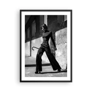 Plakat i sort ramme - En kvinde i et elegant outfit med en stok mod en baggrund af barsk arkitektur - 50x70cm -  Byens elegance - Moderne vægdekoration til stue og soveværelse ARTTOR
