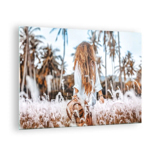Billede på glas - En kvinde i græsset med en hat i hånden mod en baggrund af palmer - 70x50cm - Født af græsdun - Moderne vægdekoration til stue og soveværelse ARTTOR