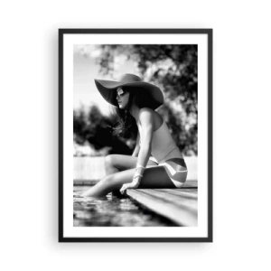 Plakat i sort ramme - Et sort-hvidt fotografi af en kvinde iført hat, der sidder ved vandet. - 50x70cm - Sommerdrøm - Moderne vægdekoration til stue og soveværelse ARTTOR
