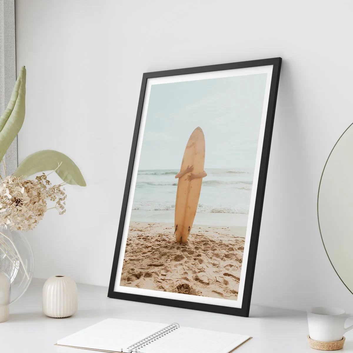 Plakat i sort ramme - En person, der holder et surfbræt på en strand med udsigt over havet. - 50x70cm - Af kærlighed til bølgerne - Moderne vægdekoration til stue og soveværelse ARTTOR
